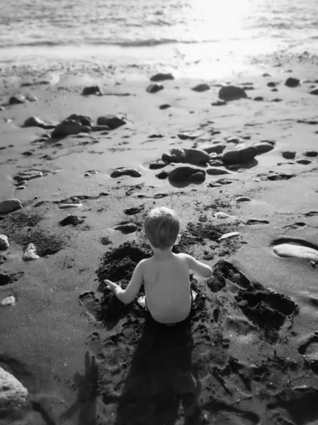 Czarny adn biały widok z tyłu obraz mały chłopiec siedzi na plaży piasek i budynek zamek — Zdjęcie stockowe