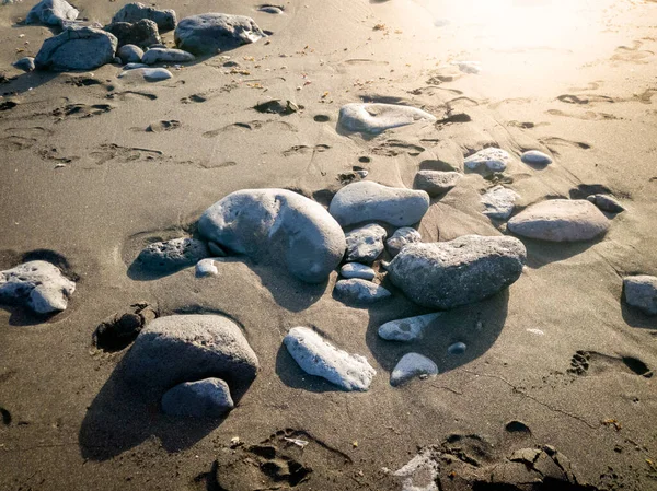 夕阳西下躺在黑沙上的鹅卵石的遮挡图像 — 图库照片