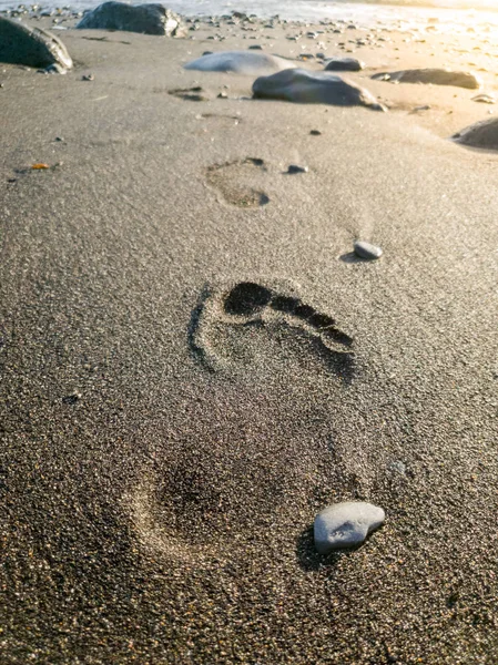 Gambar close-up jejak kaki pada pasir vulkanik hitam di pantai laut — Stok Foto