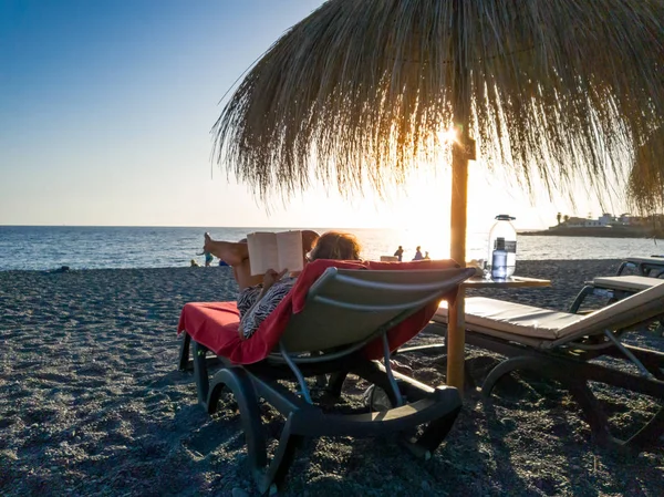 Visão traseira imagem da mulher deitada na cama de sol na praia e livro de leitura — Fotografia de Stock