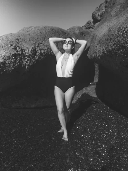 Siyah ve beyaz, güneş gözlüklü ve mayo giyen seksi bir kadın. Okyanus sahilinde güneşleniyor. — Stok fotoğraf