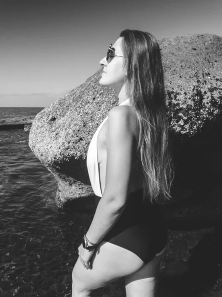 Deniz kıyısındaki kayalıklarda duran uzun saçlı seksi genç kadının siyah beyaz portresi. — Stok fotoğraf