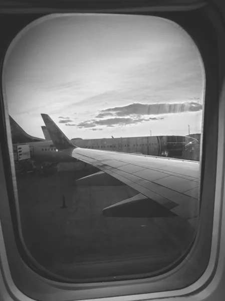 Черно-белое изображение через иллюминатор самолета на самолетах в аэропорту — стоковое фото