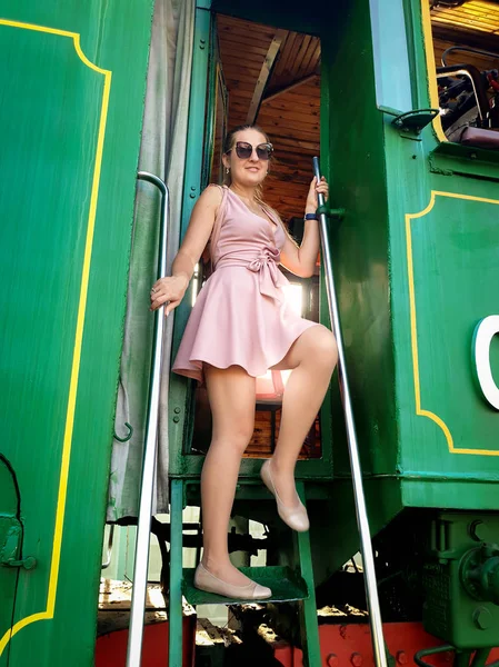 Sexy jonge vrouw in korte jurk poseren op trap van oud stoom locomotief — Stockfoto
