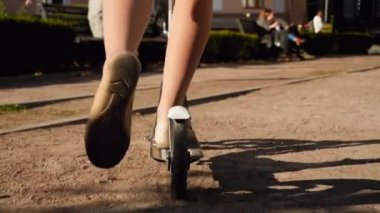 Closeup 4k video of young woman in ballet flats pushing feet while riding on scooter in city park on sunny day