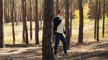4k video of happy smiling young woman with backpack hiking in autumn forest on bright sunny day