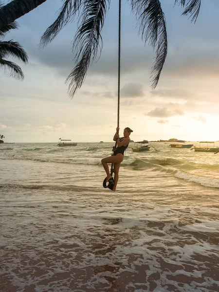 Foto di giovane donna sexy che oscilla sulla palma al tramonto sulla spiaggia — Foto Stock