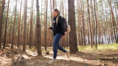 4k video of beautiful young woman with backpack walking over hills,holes and fallen tree logs while hiking in the forest