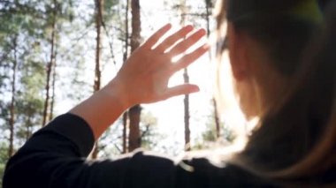 Closeup 4k video of young woman looking on bright sun through her fingers in the forest