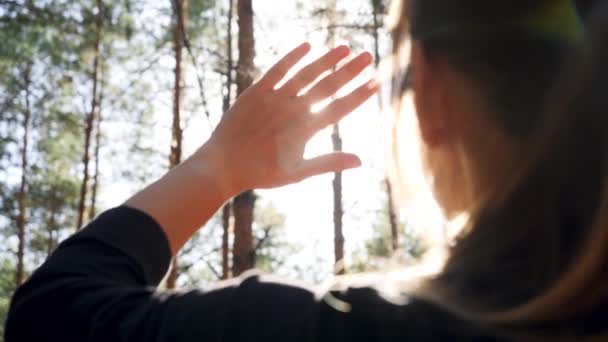 Closeup 4k vídeo de jovem mulher olhando no sol brilhante através de seus dedos na floresta — Vídeo de Stock