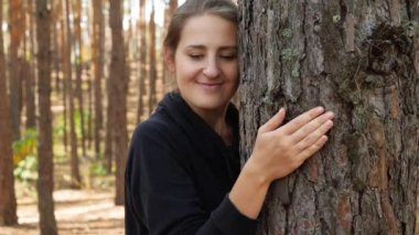 4k video of young smiling woman leaning on tree and listening to it. Concept of people loving and protecting nature