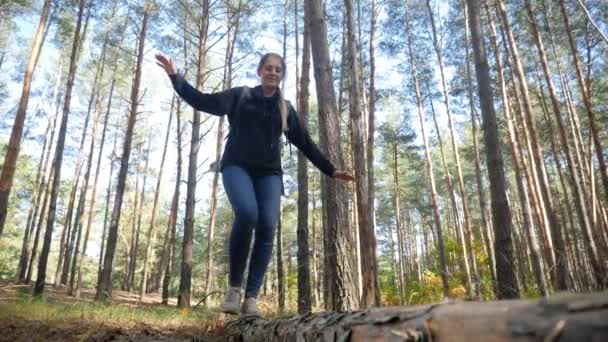 4k відео красивої молодої жінки-хокеїстки з рюкзаком, що йде над опалим деревом і балансує на великому колоді в лісі — стокове відео