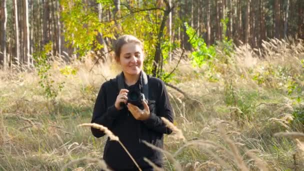 4k video of young female wildlife photographer journalist walking with camera in forest and looking for animals — Stockvideo