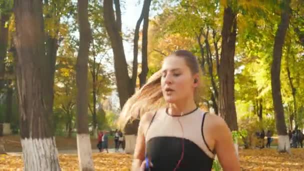 Vidéo au ralenti 4k de belle jeune femme sexy écoutant de la musique sur smartphone tout en courant au parc d'automne — Video