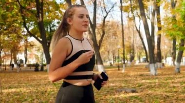 4k slow motion video of beautiful sporty woman putting earphone in ear and jogging at autumn park