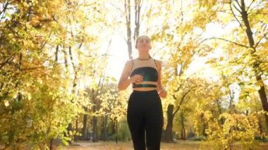 View from low point of beautiful young girl runnin on long alley under trees with golden leaves at autumn park