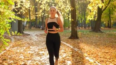 4k video of beautiful young woman in sexy sports unifor running on the pathway at autumn park under big trees