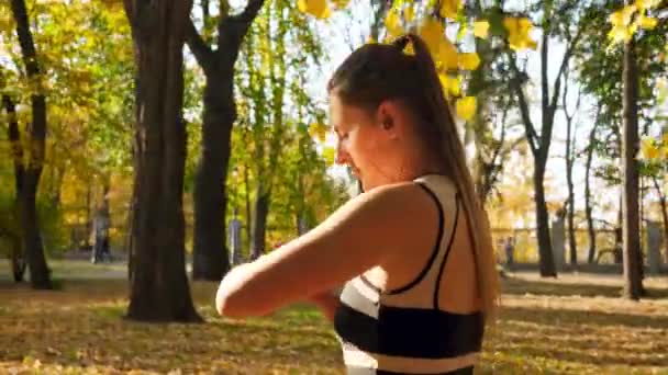4k повільне відео руху молодої красивої жінки, що використовує та встановлює розумний годинник для фітнесу під час бігу та вправ у парку — стокове відео