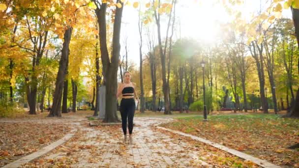 4k video wanita muda yang cantik memonitor detak jantungnya pada jam tangan kebugaran pintar saat joging di taman — Stok Video