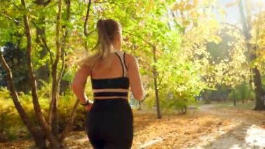 4k slow motion video of beautiful young woman drinking water from bottle while jogging and doing sports at autumn park
