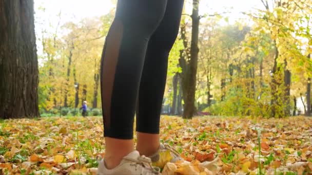 4k video of camera slowly moving from feet to head of sporty young woman drinking water from botttle after doing sports and fitness exercise at autumn park — Stockvideo