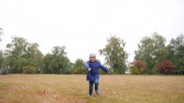 4k footage of cheerful smiling and laughing boy running on dry grass on the field at cold autumn day