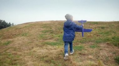 4k video of cheerful little boy holding toy airplane and running on the hill top at park