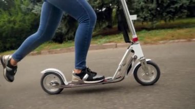 Closeup 4k video of female feet standing on scooter and riding on pathway at park