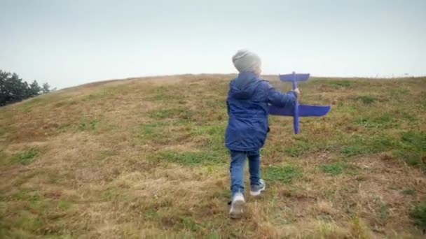 4k video of cheerful little boy holding toy airplane and running on the hill top at park — Stok video