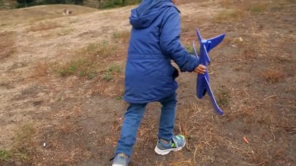 Slow motion video of little boy climbing on the hill and launching toy flying airplane at park — Stock video