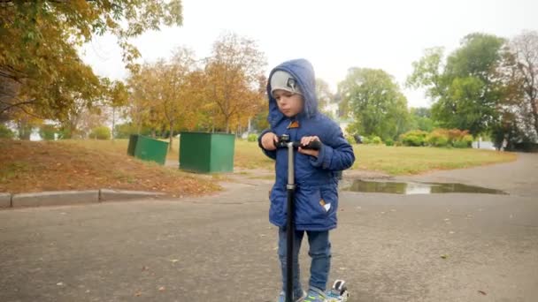 4k vídeo de chateado e triste menino andando de bicicleta no parque no frio dia de outono chuvoso — Vídeo de Stock