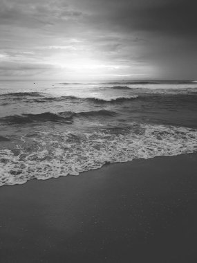 Sakin okyanus dalgaları ve kumlu plajda güneşin doğuşunun siyah ve beyaz manzarası