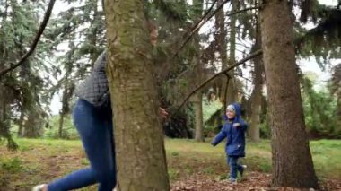 4k video of happy laughing mother with little son running between trees at autumn park and chasing each other