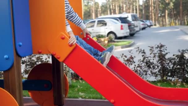 4k video de poco 4 años de edad, niño montando en pequeño tobogán en el patio de recreo — Vídeo de stock