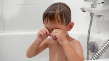 Closeup slow motion video of little boy rubbing eyes and feeling pain in eyes while washing in bath