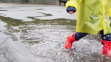 Slow motion closeup video of child in red rubber boots walking over big puddles at park and splashing water. Child having fun while raining