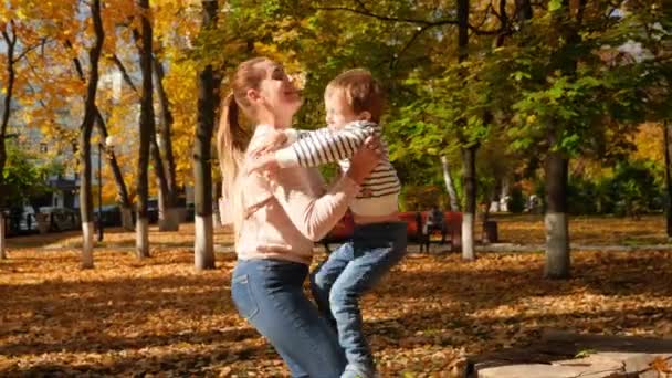Vidéo 4k de joyeuse jeune mère riant caressant son petit fils après le saut et le filant dans le parc d'automne 