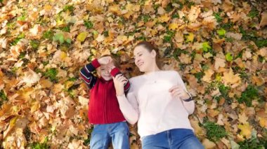 4k video of happy smiling and laughing little boy with young mother lying on grass and leaves at autumn park