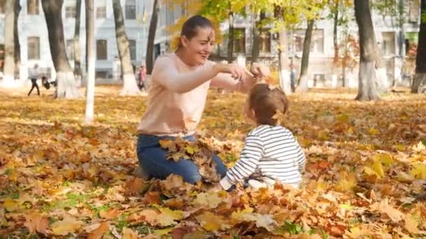 4k кадров счастливого смеющегося маленького мальчика, дерущегося со своей матерью с опавшими листьями в осеннем парке — стоковое видео