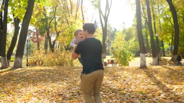 4k video of happy young father holding his little son and circling him in autumn park — Stockvideo