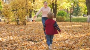 4k video of cheerful little boy running to young mtoher and autumn park and embracing her
