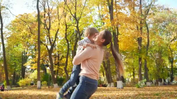 4k video of happy smiling mother lifting up, throwing in air and spinning her little toddler son at autumn park — Stockvideo