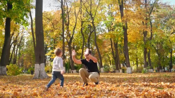 Vidéo 4k de joyeux petit garçon souriant courant vers le sien, lui donnant cinq et étreignant dans le parc d'automne 