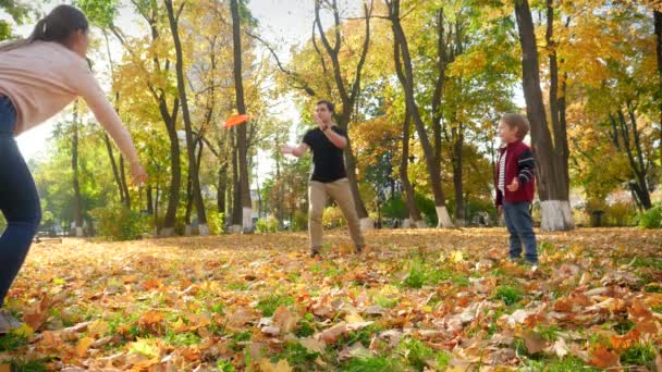 4k video of mother, father and little son playing in park. Family playing frisbee in autumn forest — Wideo stockowe