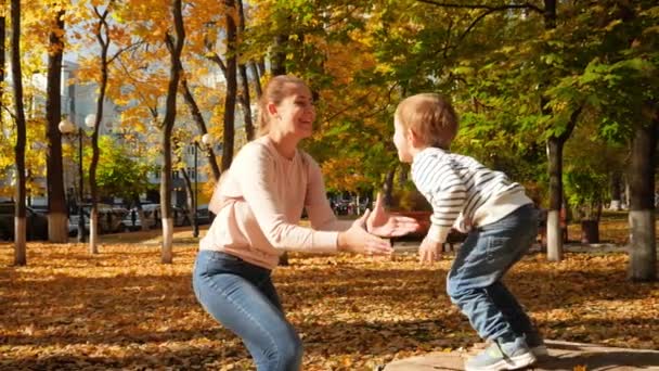 Vidéo au ralenti d'un petit garçon souriant et riant sautant de la souche de l'arbre à sa mère et l'embrassant dans un parc d'automne 
