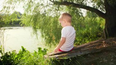 4k footage of 4 years old little boy sitting at lake and feeding fishes with bread