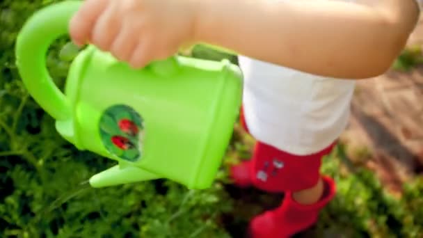 Closeup 4k footage of little boy pouring water on ground from green plastic watering can — ストック動画