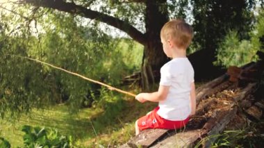4k video of little toddler boy sitting on the lake side and catching fish with selfmade fishing rod
