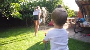 4k slow motion video of little toddler boy playing with two girls with water garden house at backyard