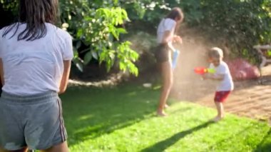 4k footage of happy laughing family playing with water guns and garden hose on grass at house backyard